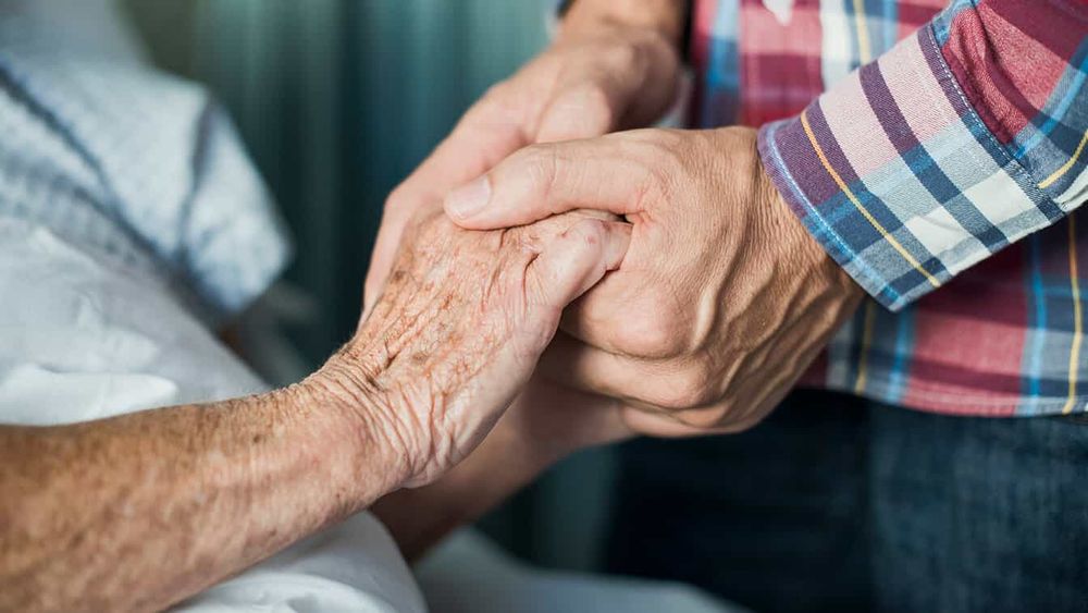 Caregiver holding hands of patient, who is showing signs of muscle wasting