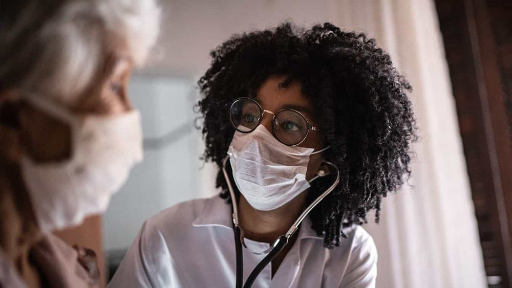 HCP with dark curly hair and glasses talking with her elderly patient