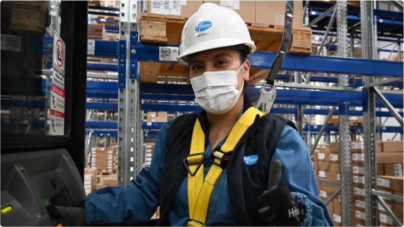 Photograph of Maritza Lopez, Warehouse Inspector, Mexico in the warehouse. She is wearing a hard hat, mask and other safety items while standing inside of warehouse