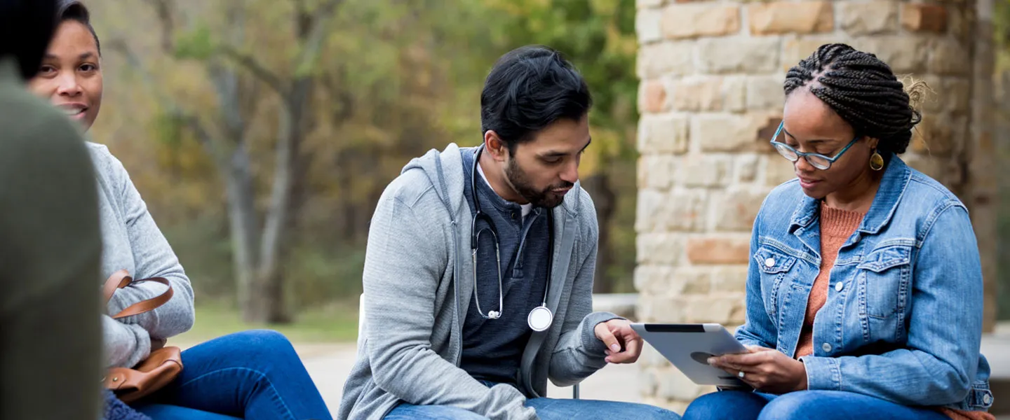 The volunteer doctor at the free clinic takes time to help a mid adult woman answer the questions on the digital tablet.